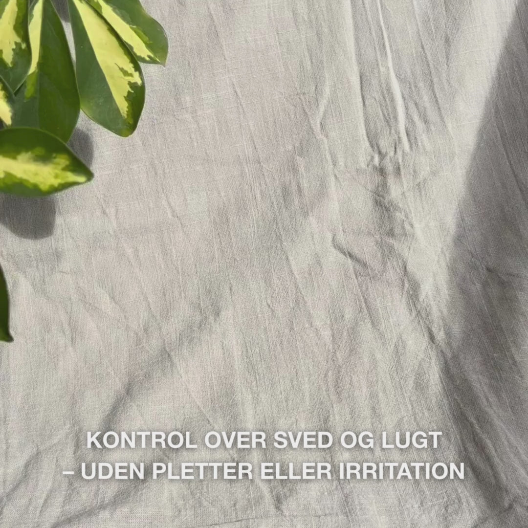 Close-up af en hånd, der ruller den klare, gel-lignende deodorant i roll-on-form på ren hud under armen: den glatte, hurtigttørrende tekstur glider blidt, danner en antiperspirant barriere, beroliger, fugter og efterlader huden frisk og uden rester.