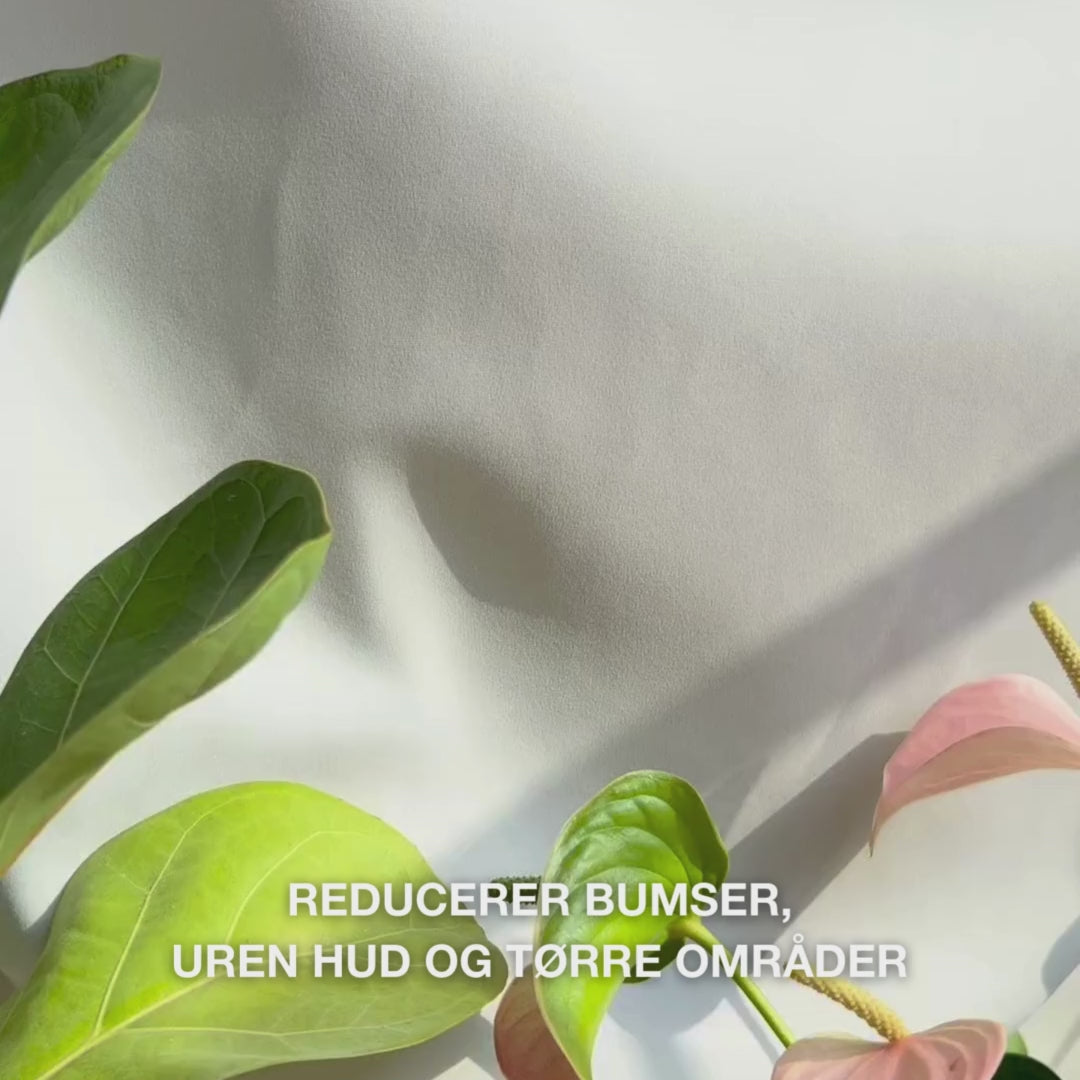 Close-up af en hånd, der doserer en lille mængde let, cremet Body Lotion med salicylsyre i håndfladen og masserer den ind i ru, uren hud: dens glatte, hurtigt absorberende tekstur eksfolierer blidt døde hudceller, fugter med hyaluronsyre og mælkesyre og forbedrer hudstruktur med salicylsyre og niacinamid.