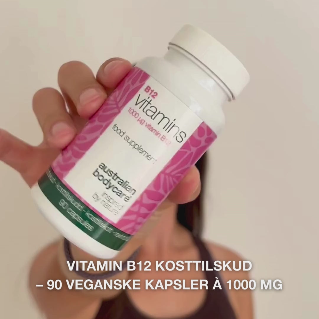 Close-up af en hånd, der holder Vitamin B12 kosttilskud, åbner låget og hælder glatte, hvide kapsler ud – viser produktet til daglig brug for energi, immunforsvar, nervesystem og reduktion af træthed.