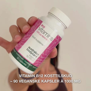 Close-up af en hånd, der holder Vitamin B12 kosttilskud, åbner låget og hælder glatte, hvide kapsler ud – viser produktet til daglig brug for energi, immunforsvar, nervesystem og reduktion af træthed.