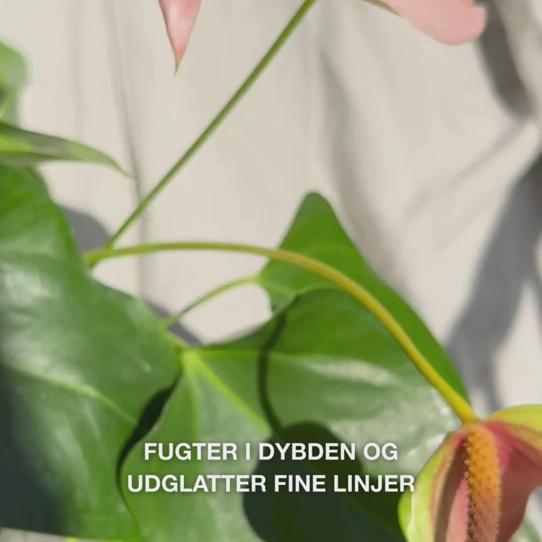 Close‑up af en hånd, der påfører et par dråber silkeagtig, klar serum fra en glastud på fingerspidserne og blidt masserer det ind i fugtig hud – den lette, hurtigt absorberende konsistens fugter øjeblikkeligt, udfylder fine linjer og beroliger med 2 % hyaluronsyre, vitamin B5 og Tea Tree Oil 