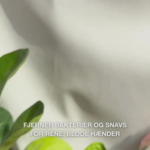 Close‑up af hænder, der pumper klar, lyseblå, skummende flydende håndsæbe med Tea Tree Oil ud i håndfladen og derefter blidt masserer den ind i håndflader, håndrygge og mellem fingrene — viser den bløde, rensende skum, der fjerner bakterier og snavs, samtidig med at den blødgør og fugter huden 